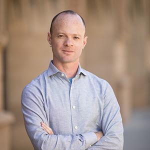 Victor Ray stands with his arms folded in a blue button down shirt.